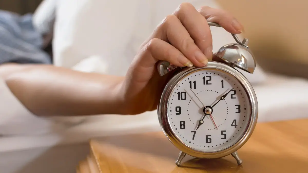 A hand touching a wooden alarm clock